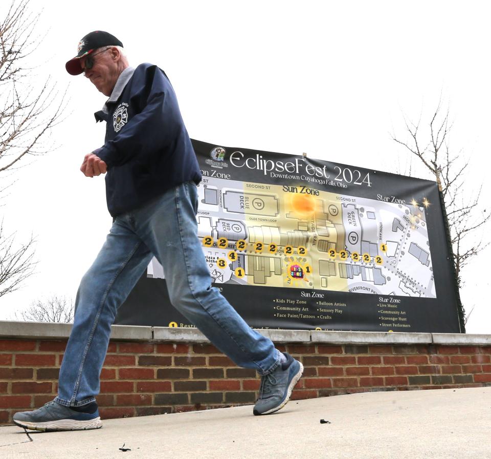 A pedestrian passes a sign advertising the upcoming EclipseFest in Cuyahoga Falls, which will feature live entertainment, food trucks and more on April 8.