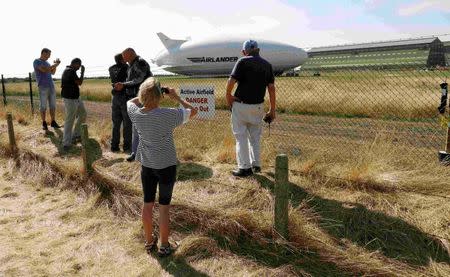 People look through the perimeter fence at the Airlander 10 hybrid airship following a crash-landing during a test flight at Cardington Airfield in Britain, August 24, 2016. REUTERS/Darren Staples