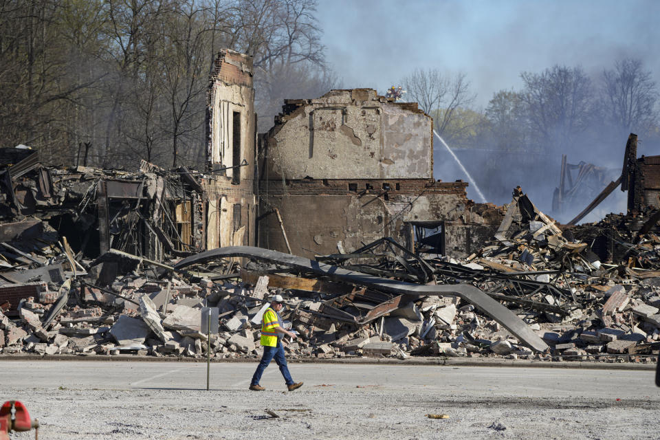 A worker walks past the rubble of an industrial fire that continued to burn in Richmond, Ind., Thursday, April 13, 2023. Multiple fires that began burning Tuesday afternoon were still burning within about 14 acres of various types of plastics stored inside and outside buildings at the former factory site. (AP Photo/Michael Conroy)