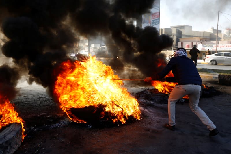 An Iraqi demonstrator burns tires to block a road during ongoing anti-government protests in Najaf