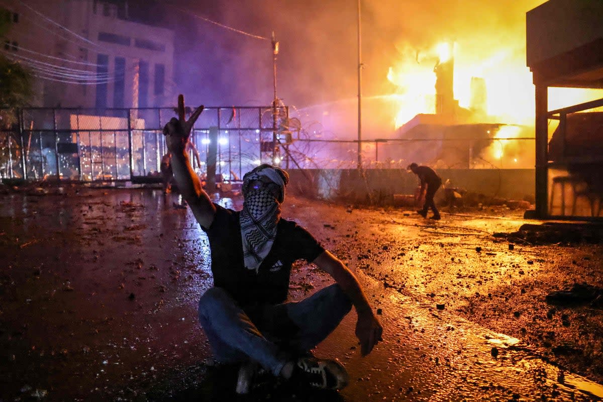 A Lebanese protester flashes the V for victory sign on October 18 as a fire rages behind the security gate of the US embassy (AFP via Getty Images)