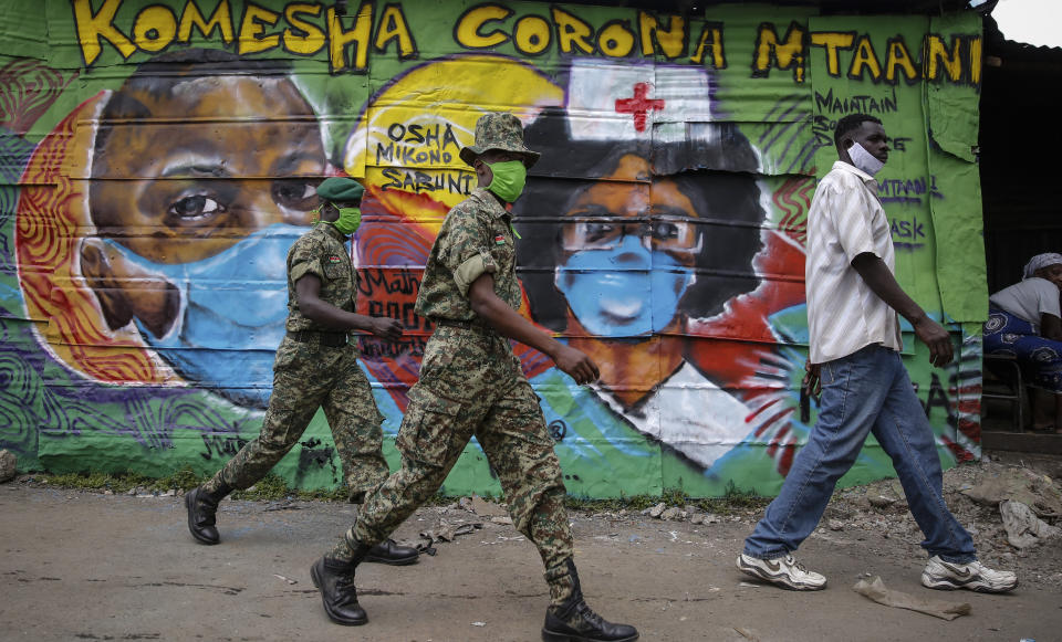 Members of the National Youth Service walk past an informational mural about the coronavirus with words in Swahili reading "Stop corona in the neighborhood", painted by graffiti artists from the Mathare Roots youth group, in the Mathare slum, or informal settlement, of Nairobi, Kenya Thursday, April 30, 2020. (AP Photo/Brian Inganga)