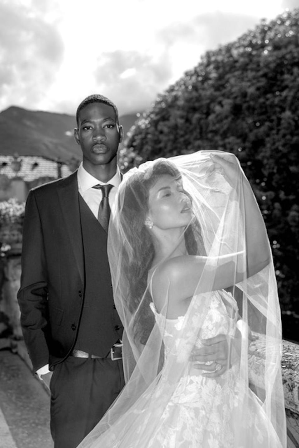 A black and white photo of a bride and groom, with the bride covering her face with her veil.