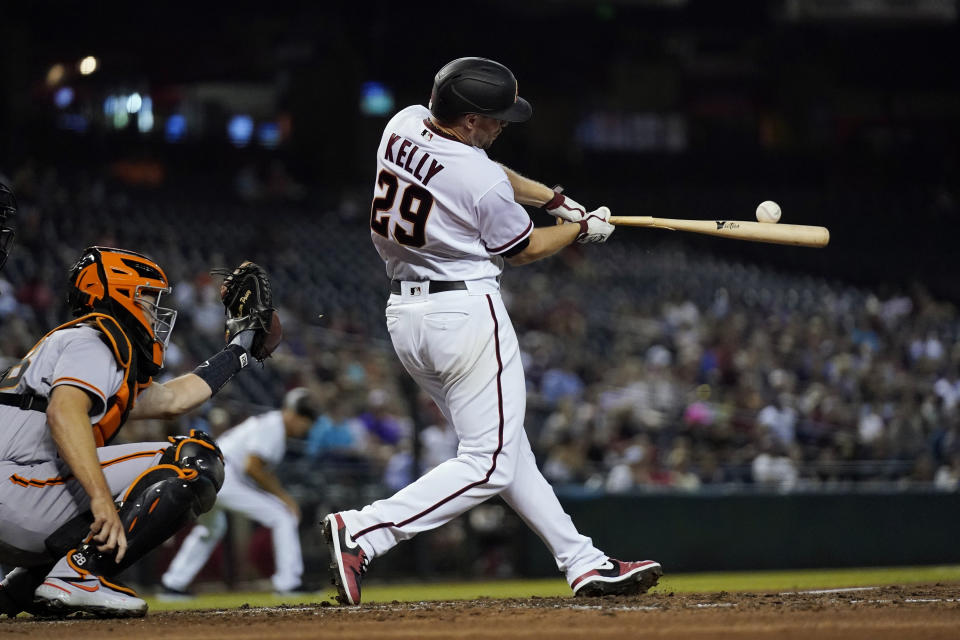 Arizona Diamondbacks' Merrill Kelly hits an RBI single next to San Francisco Giants catcher Buster Posey during the second inning of a baseball game Thursday, July 1, 2021, in Phoenix. (AP Photo/Ross D. Franklin)