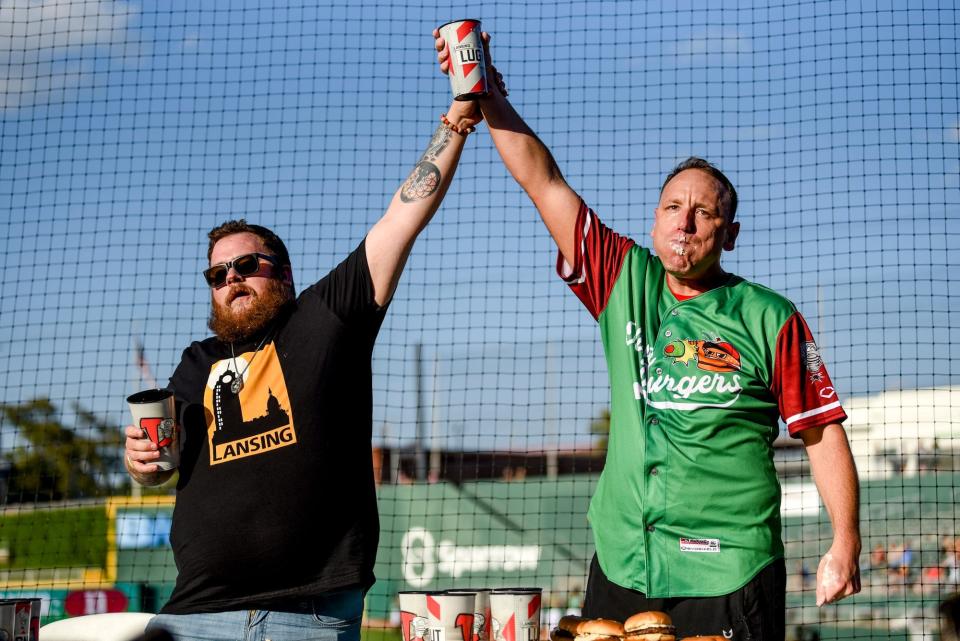 Competitive eater Joey Chestnut, right, celebrates after eating 13 olive burgers in five minutes before a minor league baseball game at Jackson Field in Lansing, Michigan on Aug. 10, 2023.