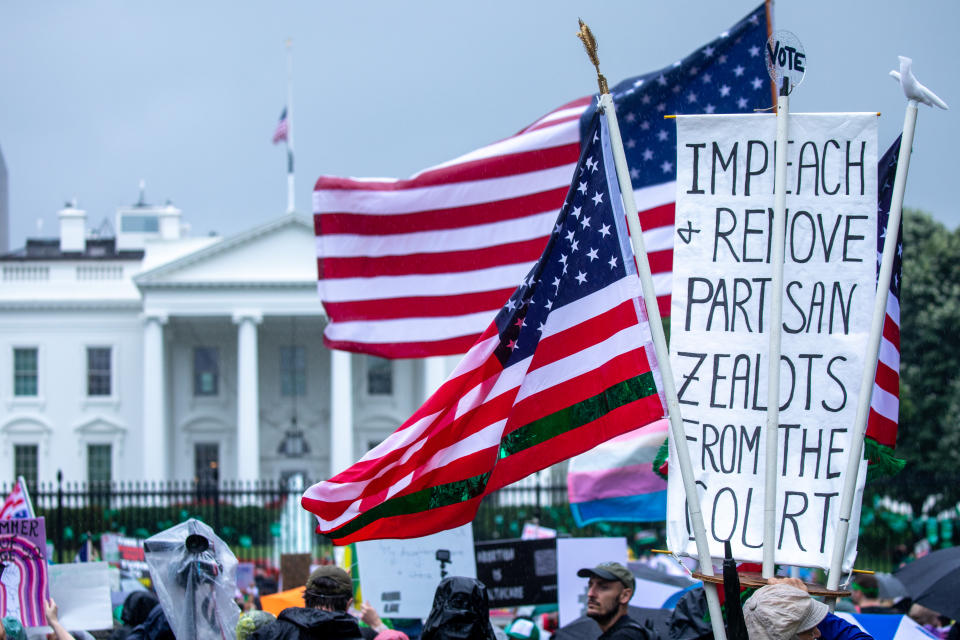 People stand in front of the White House fence holding American flags and a sign reading: Impeach and removed partisan zealots from the court.