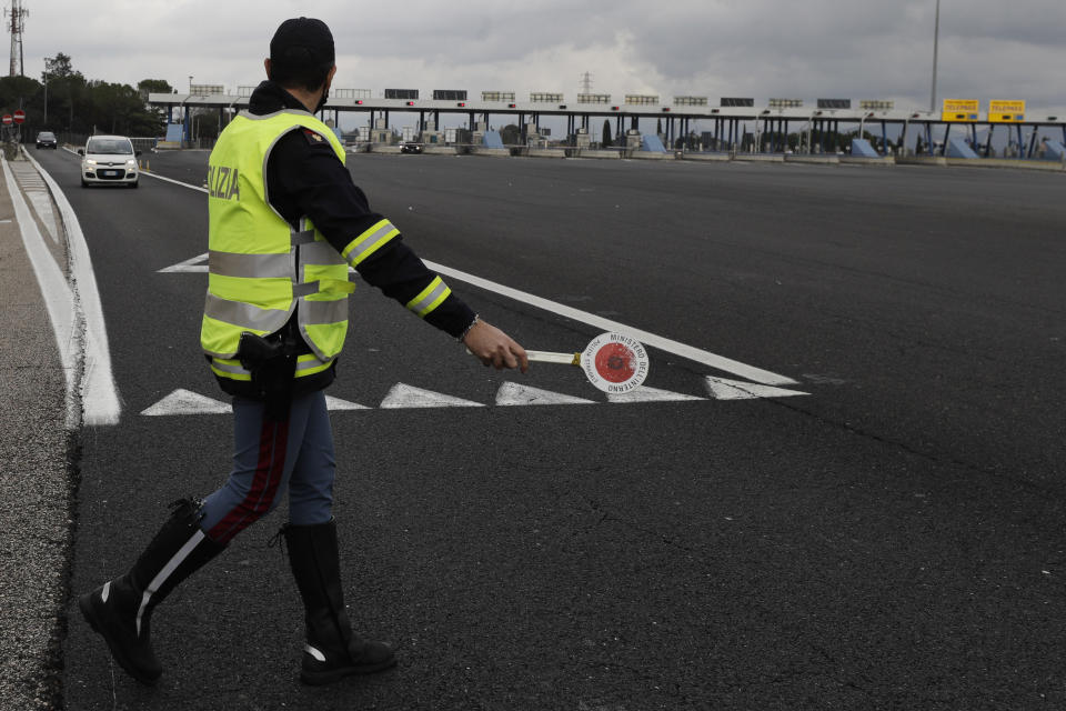 An Italian Police officer stops a car leaving the highway to enter Rome, Thursday, Dec. 24, 2020. Italians are easing into a holiday season full of restrictions, and already are barred from traveling to other regions except for valid reasons like work or health. Starting Christmas eve, travel beyond city or town borders also will be blocked, with some allowance for very limited personal visits in the same region. (AP Photo/Gregorio Borgia)