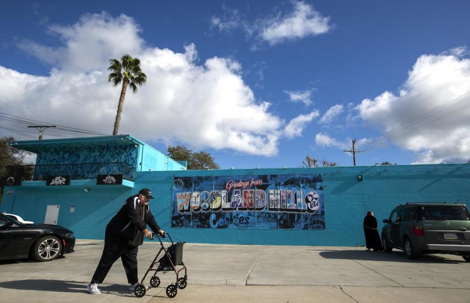 A pedestrian walks past a mural located on the wall of a cannabis dispensary on Alhama Drive in Woodland Hills.