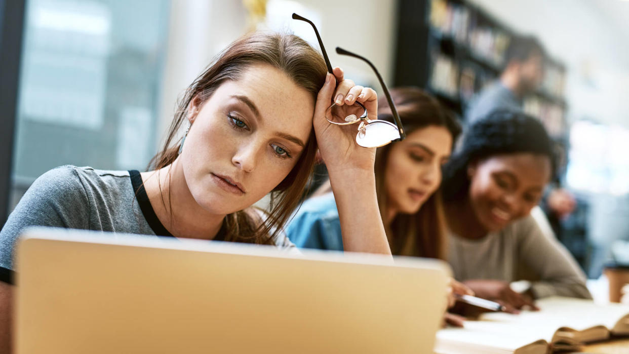 Shot of a young woman using a laptop in a college library and looking stressed.