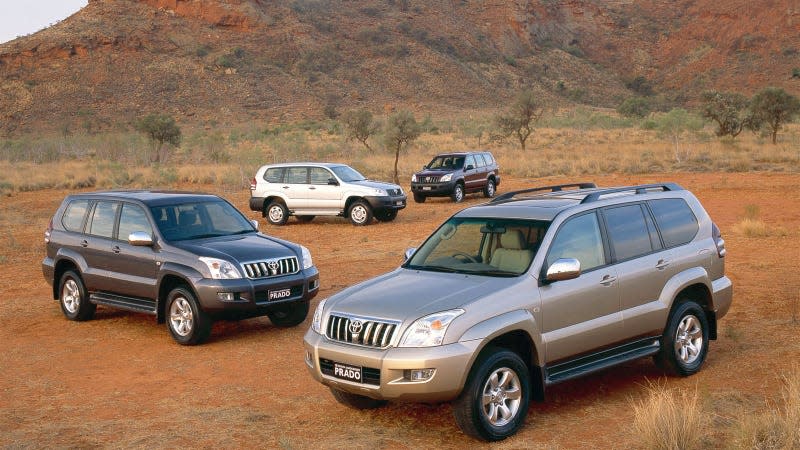 A photo of four Toyota Land Cruiser Prado SUVs parked on sand. 