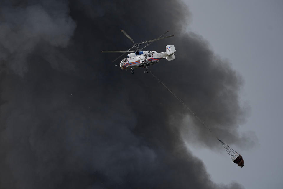 A helicopter works to extinguish fire at burning warehouse of the online retailer Ozon in Istra Municipal District, northwest Moscow Region, Russia, Wednesday, Aug. 3, 2022. The fire, which erupted at the warehouse belonging to Russia's leading online retailer Ozon, has covered the area of 50,000 square meters and injured 11 people, two of whom were hospitalized. (AP Photo/Alexander Zemlianichenko)