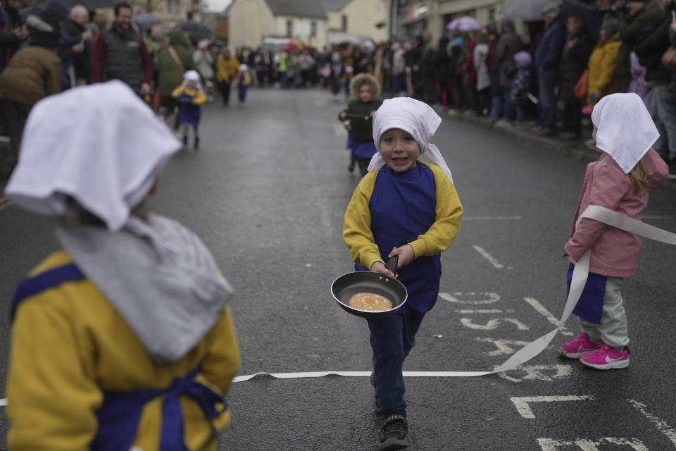 Schoolchildren from local schools take part in the children's races prior to the annual Pancake race in the town of Olney, in Buckinghamshire, England, Tuesday, Feb. 13, 2024. Every year women clad in aprons and head scarves from Olney and the city of Liberal, in Kansas, USA, run their respective legs of the race with pancakes in their pans. According to legend, the Olney race started in 1445 when a harried housewife arrived at church on Shrove Tuesday still clutching her frying pan with a pancake in it. (AP Photo/Kin Cheung)