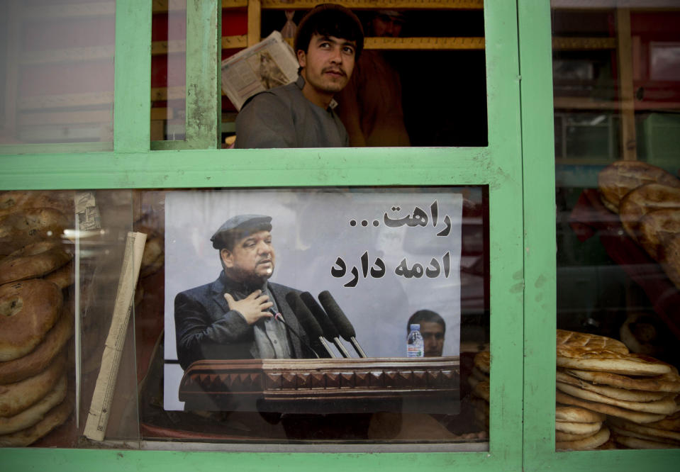 An Afghan shop keeper looks out of his bakery shop decorated with a picture of late Afghan Vice President Field Marshal Mohammed Qasim Fahim in Kabul, Afghanistan, Monday, March 10, 2014. The placard reads "we are following your way." Afghanistan's influential Vice President Fahim, a leading commander in the alliance that fought the Taliban who was later accused with other warlords of targeting civilian areas during the country's civil war, died March 9, 2014. He was 57. (AP Photo/Anja Niedringhaus)