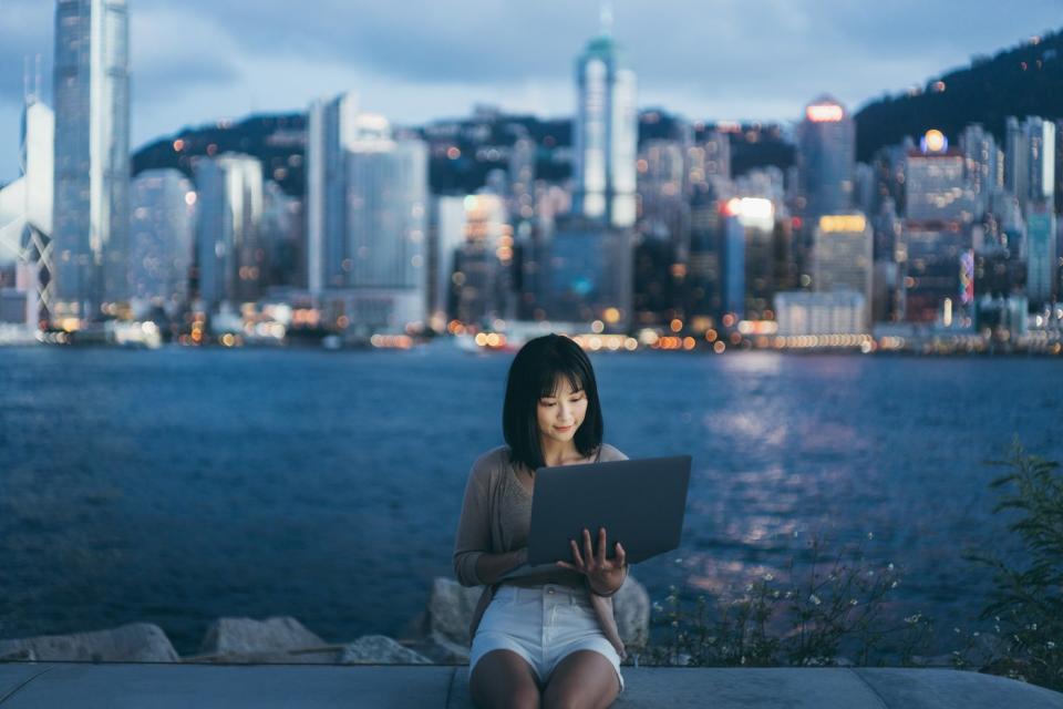 A woman on her laptop in front of the Hong Kong skyline.