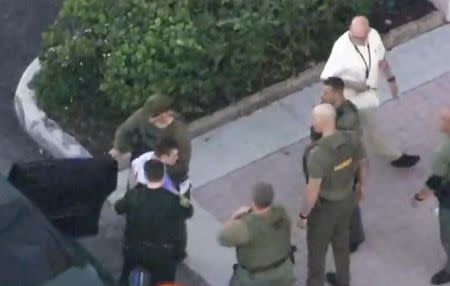 Police escort a suspect into the Broward Jail after checking him at the hospital following a shooting incident at Marjory Stoneman Douglas High School in Parkland, Florida, U.S. February 14, 2018 in a still image taken from a video. WSVN.com via REUTERS