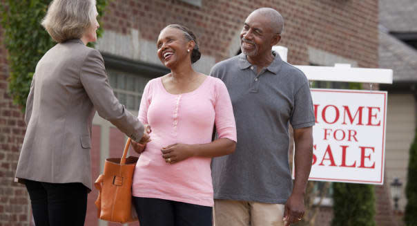 Realtor shaking hands with smiling couple outside house for sale