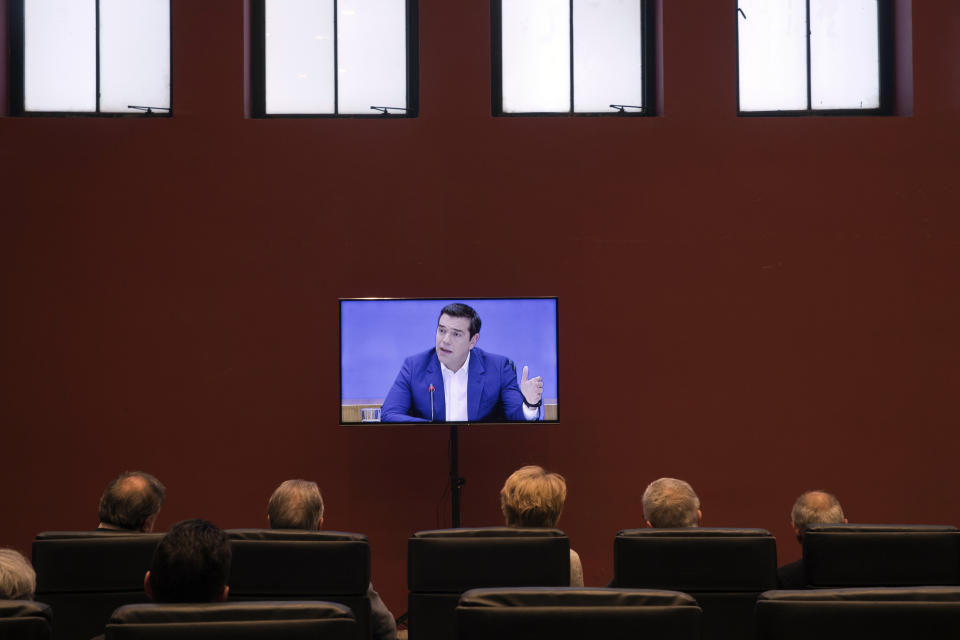 People watch a TV screen as Greek Prime Minister Alexis Tsipras announces bailout relief measures during a press conference, in Athens, on Tuesday, May 7, 2019. Greece's left-wing prime minister has promised crisis-weary voters a series of tax-relief measures ahead of elections, after outperforming budget targets set by bailout creditors. (AP Photo/Petros Giannakouris)