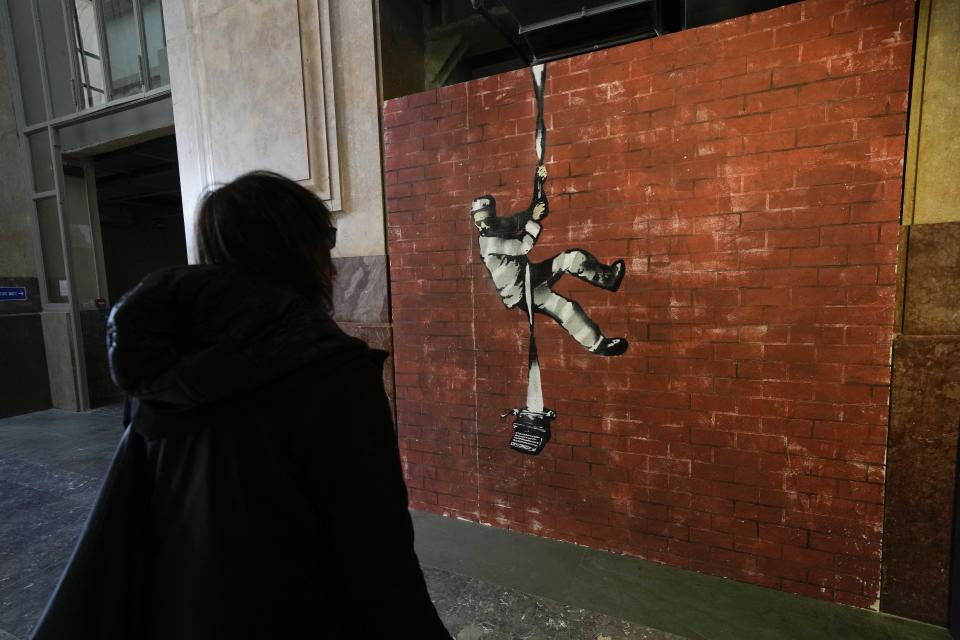 A visitor walks past "Create Esacape", a reproduction of a mural by British artist Banksy, during the unveiling of the "The World of Banksy, The Immersive Experience" exhibition, in Milan, Italy, Thursday, Dec. 2, 2021. An exhibition of 130 works by British street artist Banksy opens Friday in a gallery space inside Milan's Central train Station. The exhibition unveiled on Thursday includes 30 never before seen works by Bansky and highlights pieces by young unknown artists from all over Europe. (AP Photo/Luca Bruno)