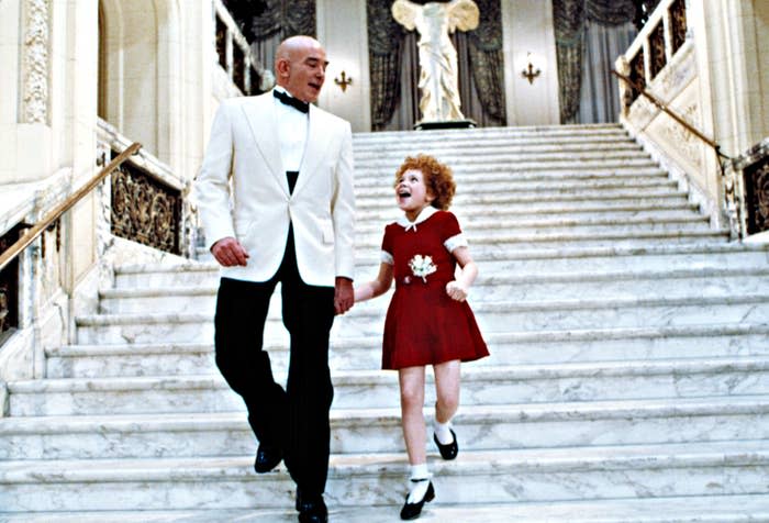 Annie and Daddy Warbucks descend a staircase while singing