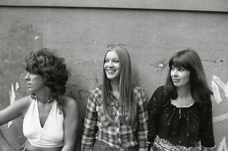 Three women stand in front of a cement wall.