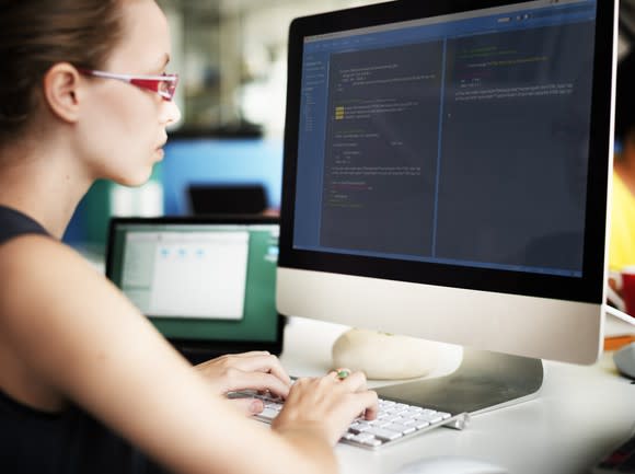 Woman sitting in front of computer screen with code on it