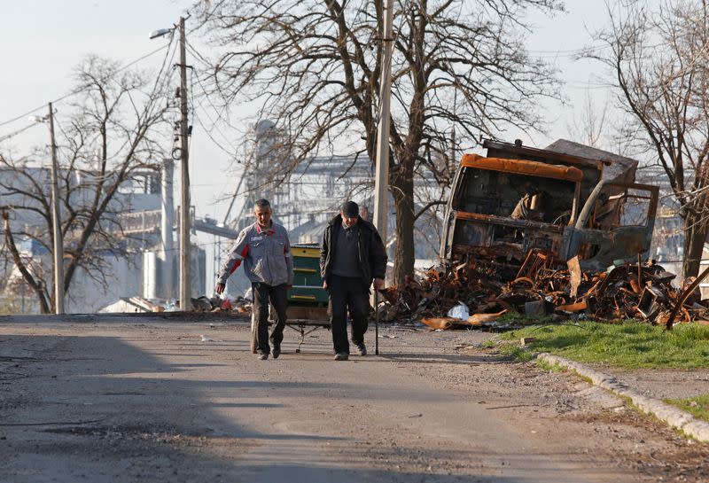Local residents walk past a destroyed vehicle in Mariupol