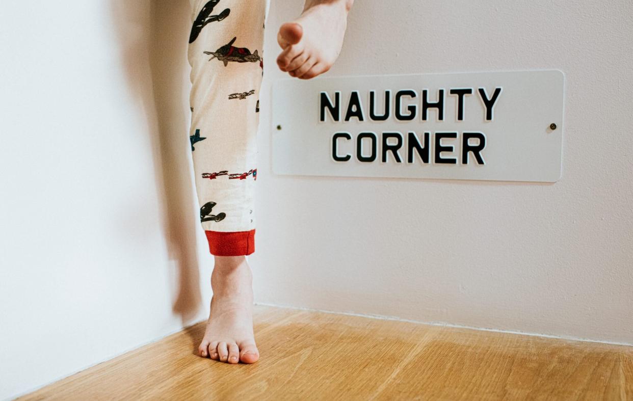 kids feet with naughty corner sign on wall