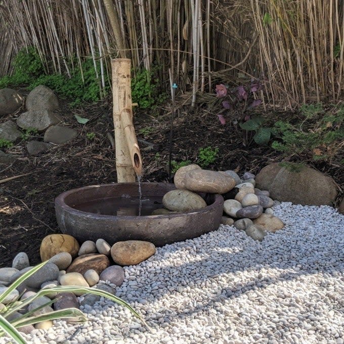 Bamboo fountain with water flowing into a round basin surrounded by smooth stones and pebbles in a garden