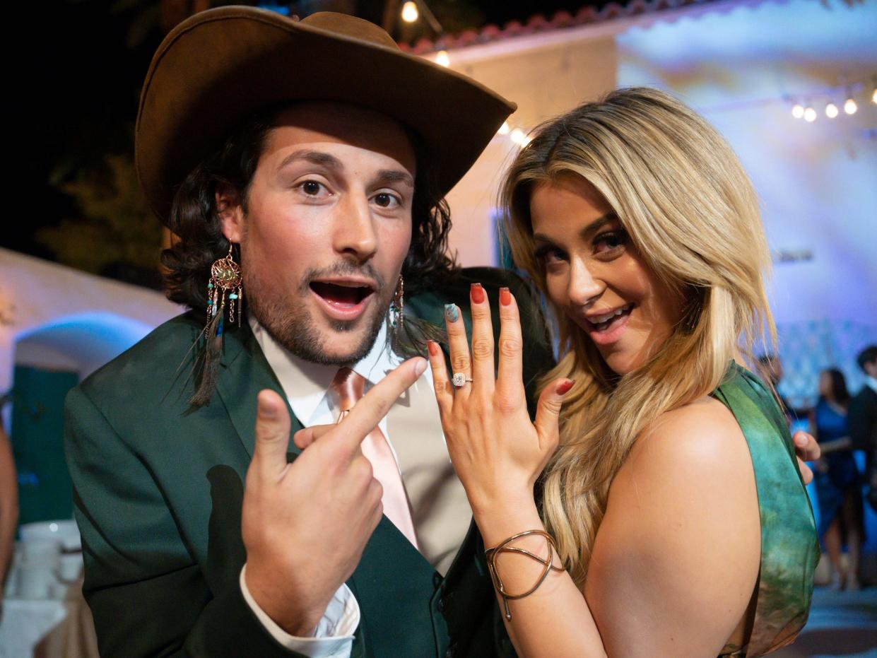 Brayden Bowers, in a green suit, grown hat, and dangly earrings, point towards Christina Mandrell's engagement ring.