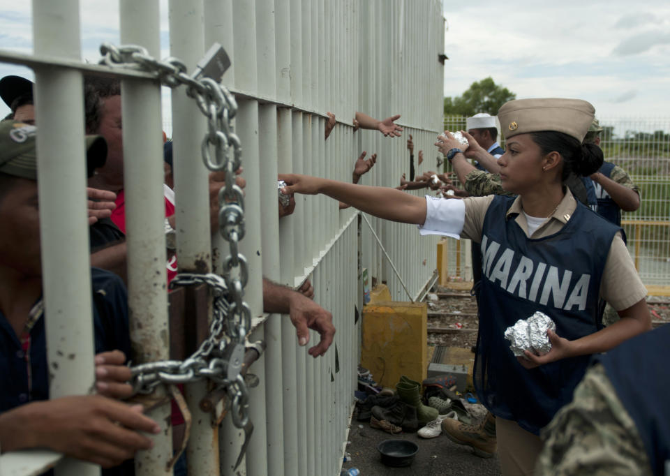 Mexican navy personnel hand out food to Central American migrants stuck in no man's land on the bridge over the Suchiate River that is the border between Guatemala and Mexico, near Ciudad Hidalgo, Mexico, Saturday, Oct. 20, 2018. The entry into Mexico via the bridge has been closed. The migrants have moved about 30 feet back from the gate that separates them from Mexican police to establish a buffer zone. About 1,000 migrants now remain on the bridge between Guatemala and Mexico. (AP Photo/Oliver de Ros)