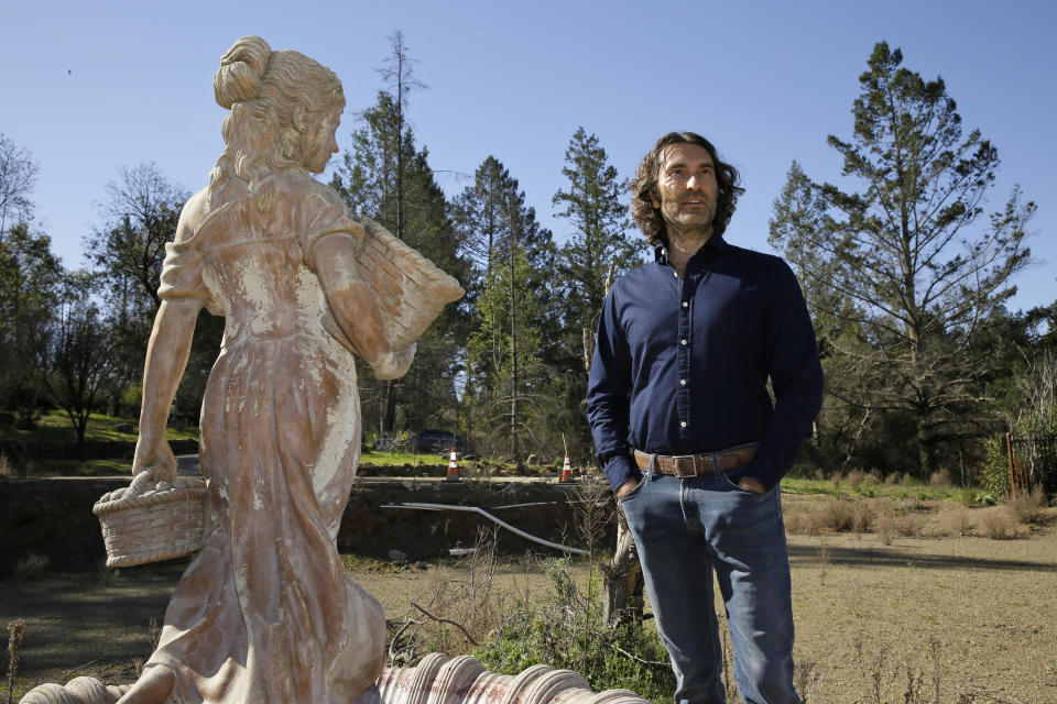 In this Tuesday, Feb. 25, 2020, photo, Jason Meek, whose Northern California wine country home was destroyed in 2017, stands by a fountain in the backyard amidst the remains of his home in Santa Rosa, Calif. A $13.5 billion settlement between victims, including Meek, of California's catastrophic wildfires and Pacific Gas & Electric was supposed to bring some peace and hope to people still reeling from the devastation. Instead, it has sparked confusion, resentment, suspicion and despair as the victims, government agencies, and lawyers grapple for their piece of the settlement fund. (AP Photo/Eric Risberg)