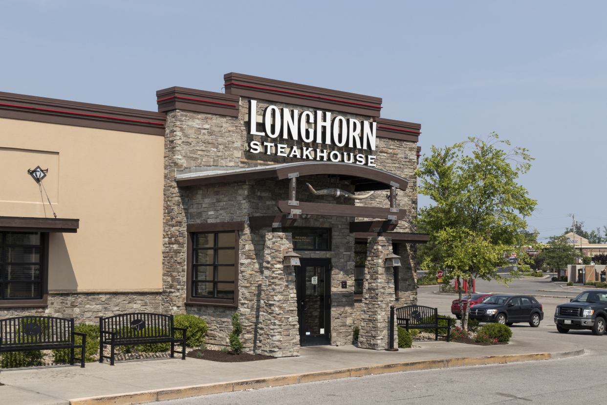 Front exterior of LongHorn steakhouse casual dining restaurant in Cincinnati, Ohio, front doors and outdoor waiting area with parking lot in the background on a sunny summer day