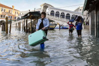 FILE - In this Monday, Dec. 23, 2019 file photo, people carry their luggage as they wade through water during a high tide of 1.44 meters (4.72 feet), near the Rialto Bridge, in Venice, Italy. Lashing winds that pushed 1.87 meters (nearly 6 feet 2 inches) of water into Venice in November 2019 and ripped the lead tiles off St. Mark’s Basilica for the first time ever shocked Venetians with the city’s second-worst flood in history, but it was the additional four exceptional floods over the next six weeks that triggered fears about the impact of worsening climate change. (AP Photo/Luigi Costantini, file)