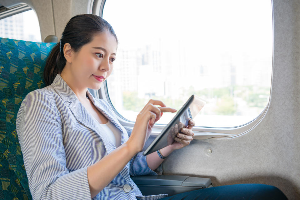 happy smile Asian business lady using mobile touchpad app and working hard on the moving train for the meeting.