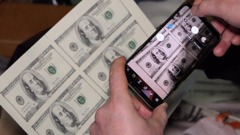 In this photo provided by Bulgaria's Interior Ministry on Tuesday, March 16, 2021, a policemen takes a photo of counterfeit money at a printing office in a university in Sofia. Bulgarian authorities say they have seized high-quality forged banknotes produced at a printing office in a university in the Bulgarian capital. In a joint operation with U.S. Secret Service, Bulgarian police detained two people and seized a printing machine and equipment for printing money, along with large amounts of counterfeit U.S. dollar and euro notes. (Bulgarian Interior Ministry via AP)