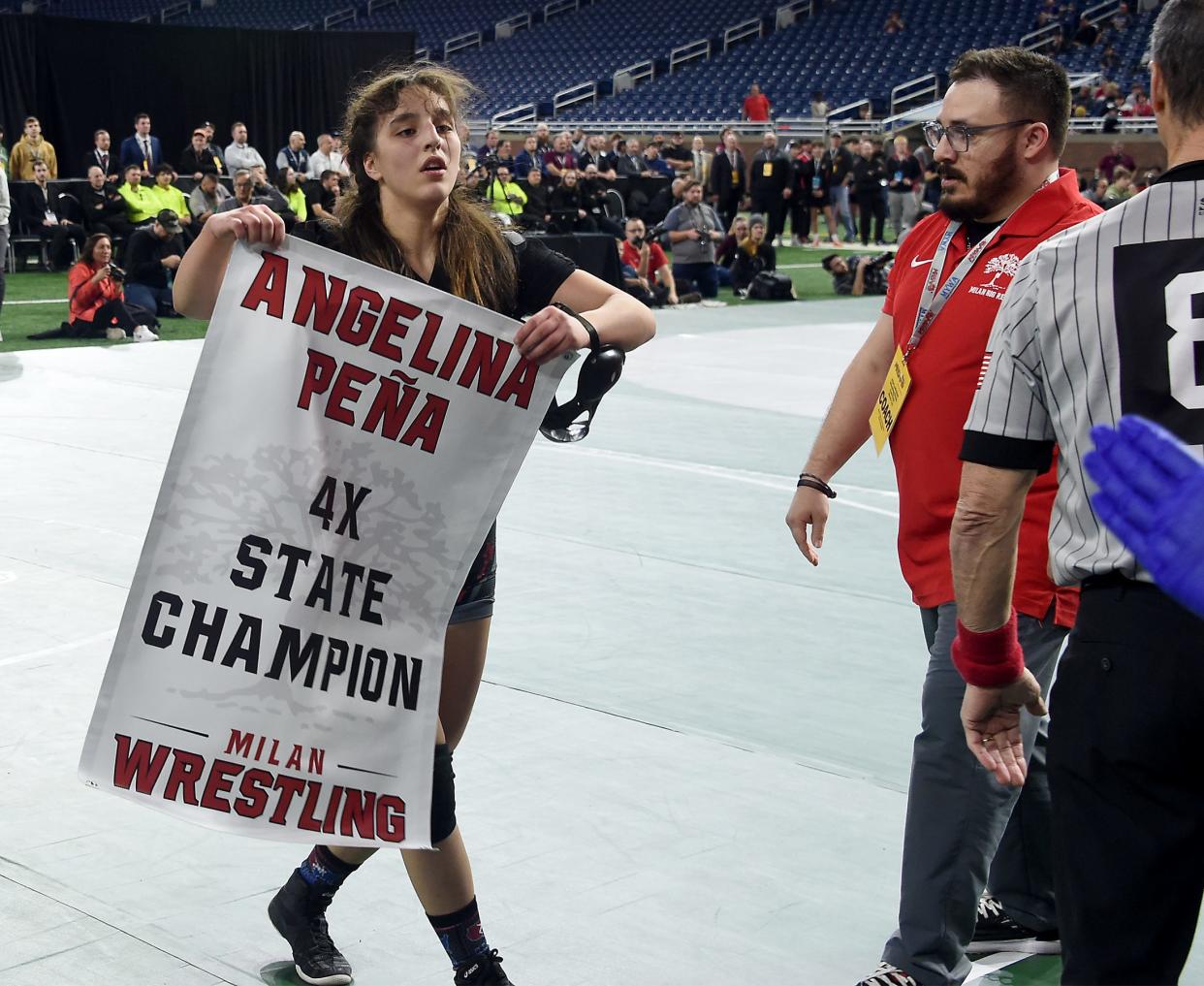 Milan's Angelina Pena won her fourth MHSAA State Individual Wrestling Championships at Ford Field in Detroit on Saturday, March 2, 2024, holds up a sign given to her by her coach Adam Caballero.