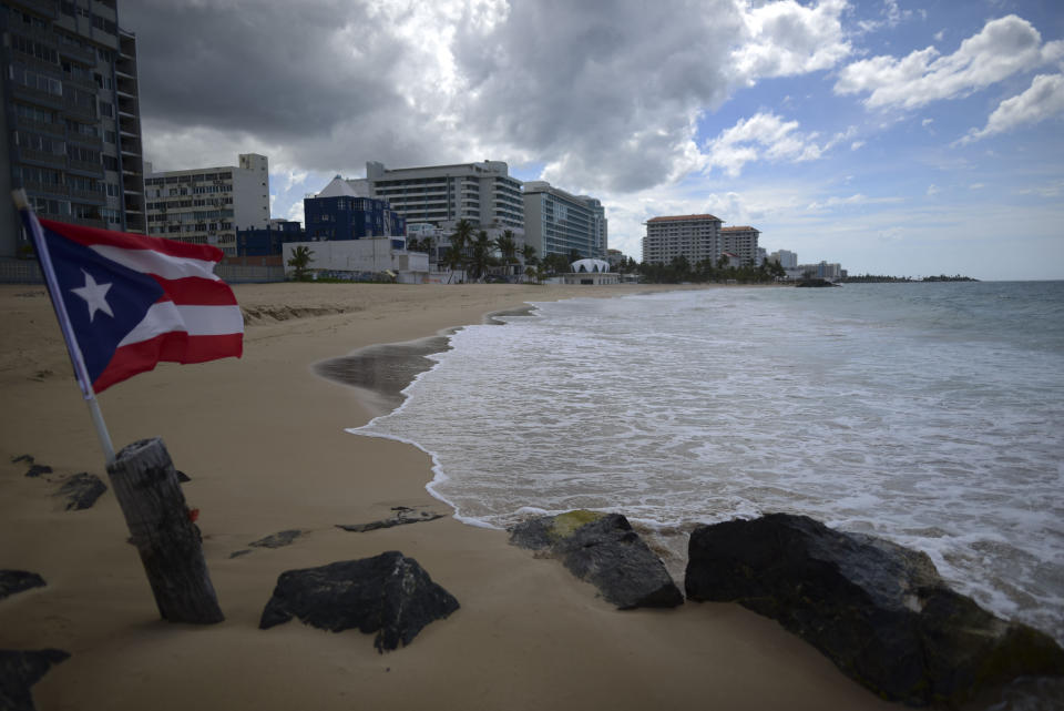 A Puerto Rican flag flies on an empty beach at Ocean Park, in San Juan, Puerto Rico, Thursday, May 21, 2020. Puerto Rico is cautiously reopening beaches, restaurants, churches, malls, and hair salons under strict conditions as the U.S. territory emerges from a two-month lockdown despite dozens of new coronavirus cases reported daily. (AP Photo/Carlos Giusti) PUERTO RICO OUT-NO PUBLICAR EN PUERTO RICO