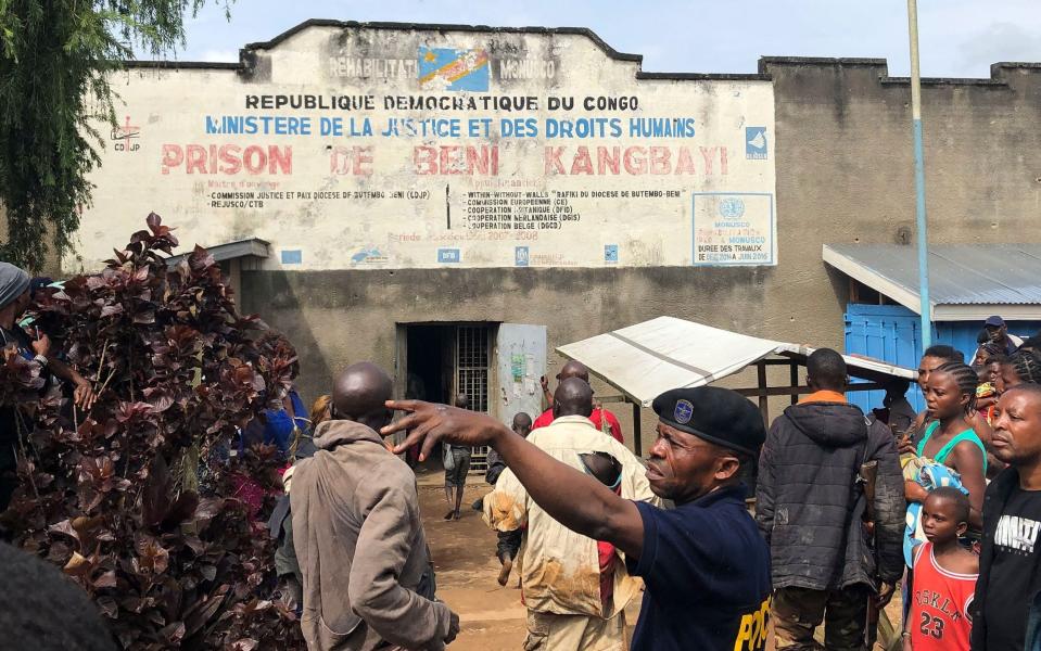 A policeman gestures as Congolese look on at the breached entrance of Kangbayi prison following a prison break  - Shutterstock