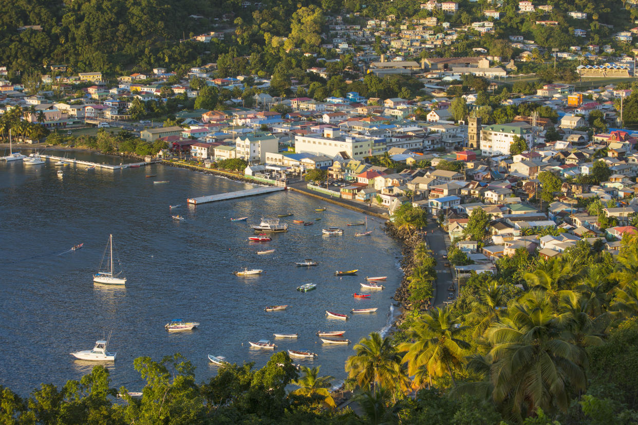 View over the waterfront from densely wooded hillside, sunset, Soufriere, Saint Lucia, West Indies, North America. Lying in the eastern Caribbean between Martinique and Saint Vincent, Saint Lucia is one of the Windward Islands, which themselves form part of the Lesser Antilles. Soufriere, the former capital of the island, boasts an enviable location on Soufriere Bay at the foot of the iconic Pitons, twin coastal peaks over 700 metres in height. The Pitons Management Area was added to the UNESCO World Heritage List in 2004.