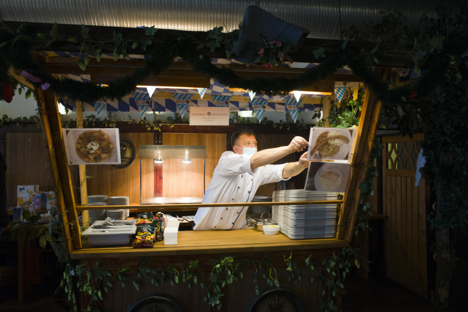 Cook Sascha Richter puts up photos of the menu at the food distribution station for the homeless people at Berlin's biggest restaurant Hofbraeu Berlin, in Berlin, Germany, Thursday, Dec. 17, 2020. The restaurant which had to closed due to the corona pandemic has opened its doors for homeless people. Starting this week the Hofbraeu Berlin offers free meals, a place to warm up and counseling for up to 150 homeless people per day. (AP Photo/Markus Schreiber)