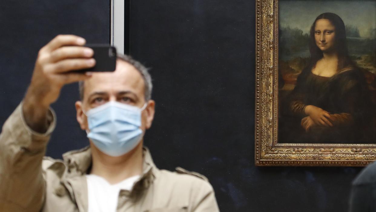 A visitor wearing a protective face mask takes a selfie in front of Leonardo da Vinci's masterpiece, "Mona Lisa," also known as "La Gioconda," on the reopening day of the Louvre Museum in Paris, France on July 6, 2020.