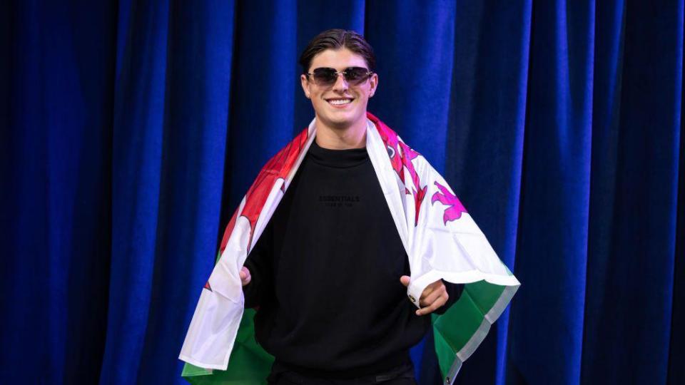 Rees-Zammit poses with the flag of Wales during the NFL Draft in April