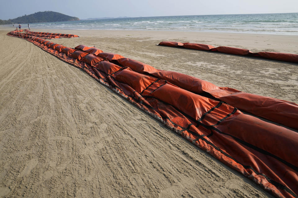 Tourists walks along Mae Ram Phueng Beach near oil spill booms laid out to try and contain any oil from a recent spill off the coast of Rayong, eastern Thailand, Friday, Jan. 28, 2022. An oil slick off the coast of Thailand continued to expand Friday and was approaching beaches on the east coast, home to fragile coral and seagrass, officials said. (AP Photo/Sakchai Lalit)