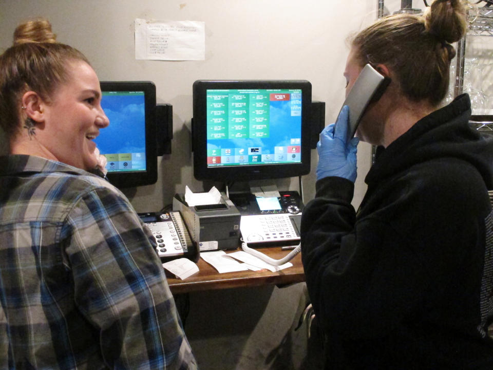 In this March 24, 2020 photo, Kirsten Phillips, left, and Sylvia Pappa, right, take telephone orders at Federico's Pizza in Belmar N.J. The owners of the business took out a $50,000 line of credit to ensure that their employees can stay on the payroll for at least two months during the virus outbreak. That prompted an outpouring of donations from customers wanting to send pizzas to hospital workers and first responders. (AP Photo/Wayne Parry)