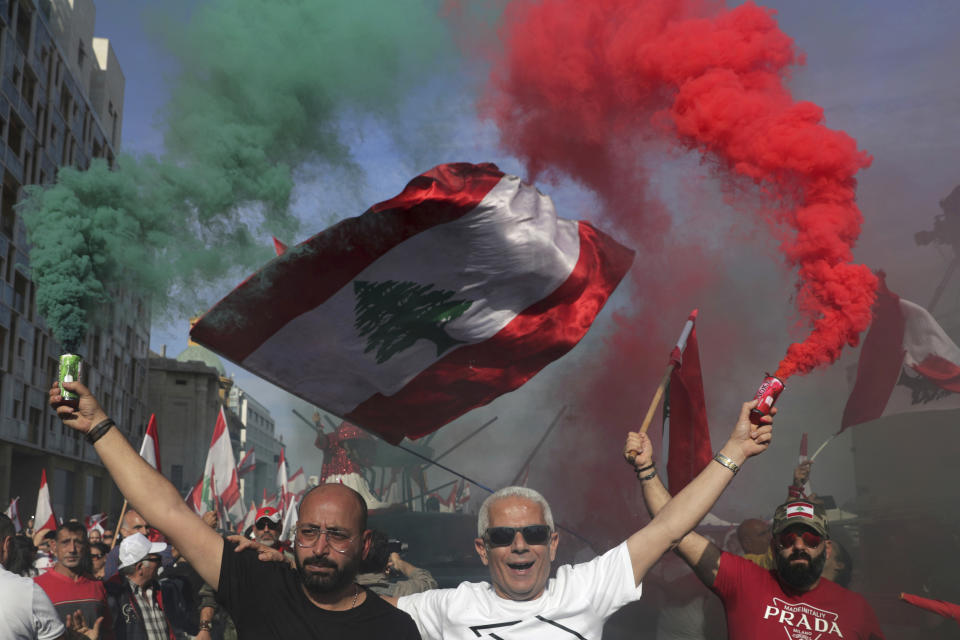 Anti-government protesters wave Lebanese national flags as hold smoke flares during separate civil parade at the Martyr square, in downtown Beirut, Lebanon, Friday, Nov. 22, 2019. Protesters gathered for alternative independence celebrations, converging by early afternoon on Martyrs’ Square in central Beirut, which used to be the traditional location of the official parade. Protesters have occupied the area, closing it off to traffic since mid-October. (AP Photo/Hassan Ammar)