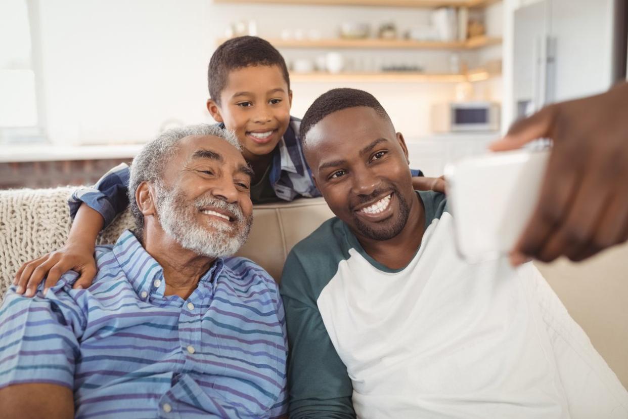 Smiling multi-generation family taking selfie from mobile phone in living room at home