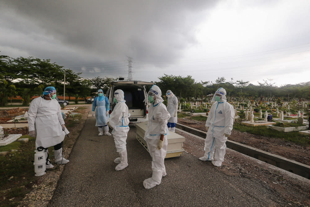 Workers and family members wearing protective suits prepare to bury a victim of the Covid-19 disease at a cemetery in Shah Alam May 18, 2021. — Picture by Yusof Mat Isa