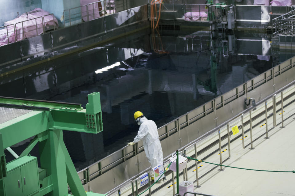 A worker for Tokyo Electric Power Co. looks at an extra cooling pool containing spent fuel from reactors at the Fukushima Daiichi nuclear power plant in Okuma town, Fukushima prefecture, northeastern Japan, Saturday, Feb. 27, 2021. (AP Photo/Hiro Komae)