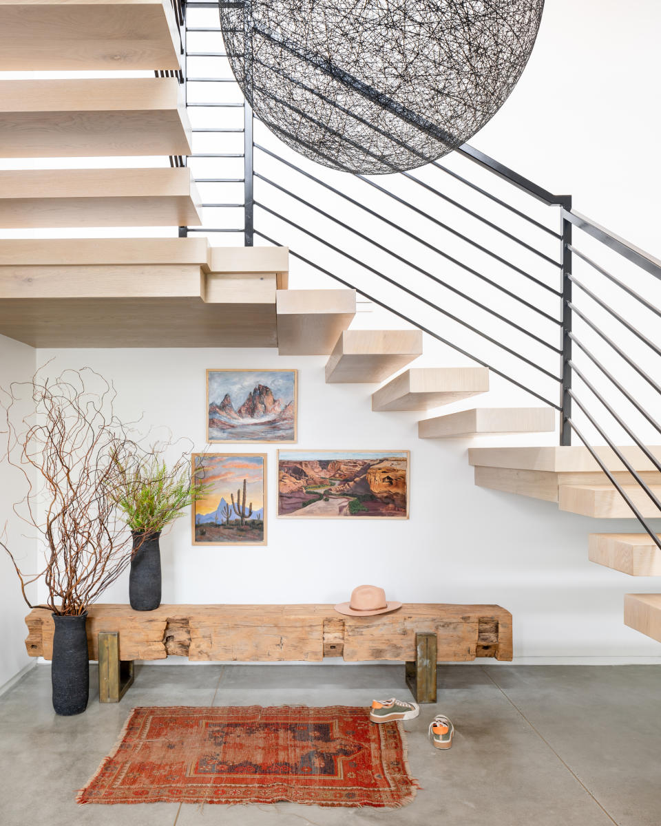 A staircase with 'floating' treads rise over a bench, rug, and framed artwork