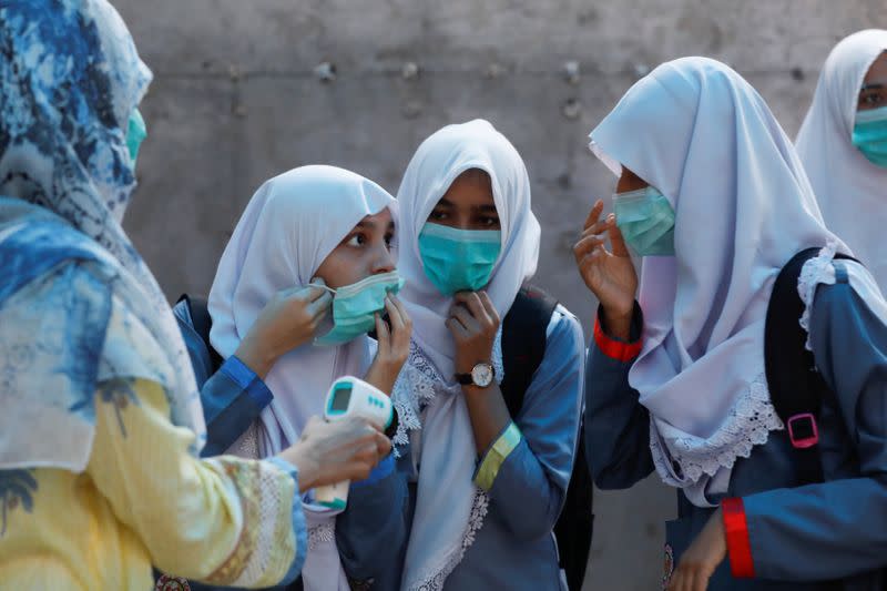 Students adjust their protective masks as they get their temperature checked before entering a class as schools reopen amid the coronavirus disease (COVID-19) pandemic, in Karachi,